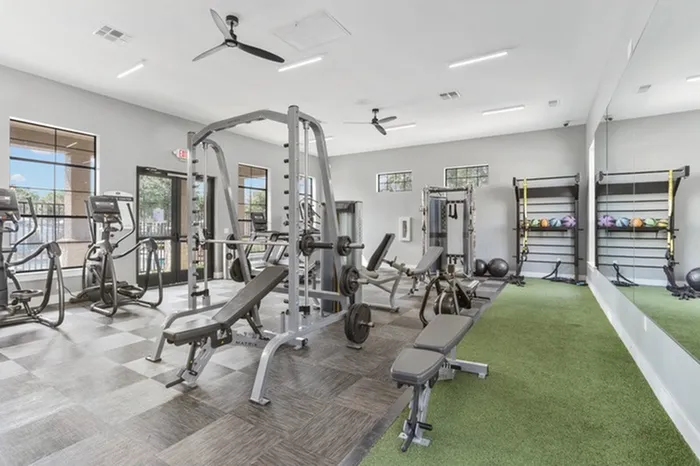 Spacious gym with a variety of gym equipment including free weights and machines, treadmills, turf area, and ellipticals all with a pool view at Lantower Residences at the Collection apartments