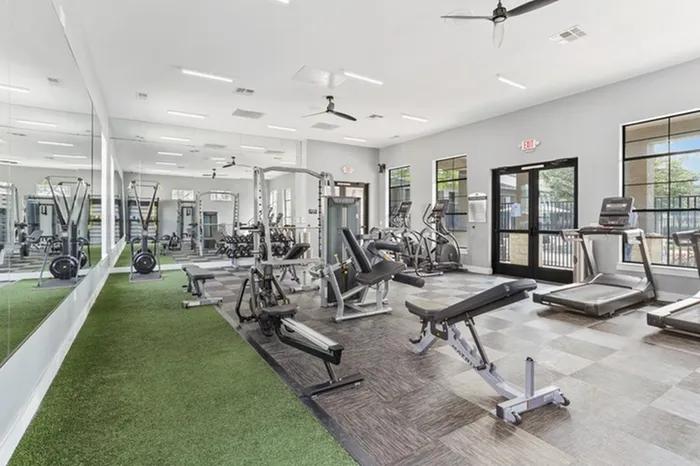 Spacious gym with a variety of gym equipment including free weights and machines, treadmills, turf area, and ellipticals all with a pool view at Lantower Residences at the Collection apartments