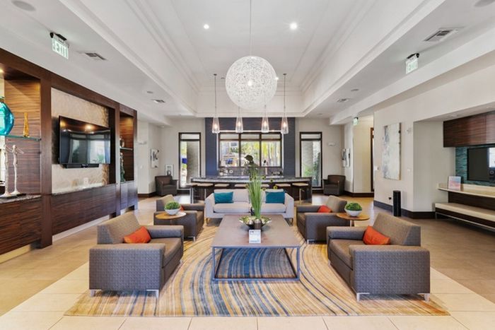 Lounge with modern furniture, wall-mounted TVs, chandeliers, and green plants and flowers on the coffee table at Lantower Brandon Crossroads Apartments.