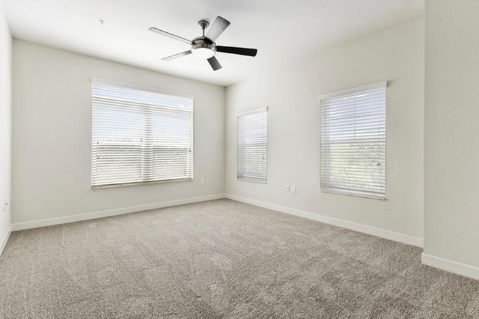 Spacious, carpeted bedroom with a ceiling fan and three large windows with ample natural light at Lantower Brandon Crossroads.