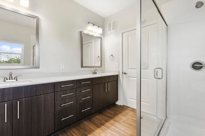 A modern, clean bathroom with dark-colored cabinetry, brushed nickel fixtures, and a walk-in, glass door shower at Lantower Brandon Crossroads.