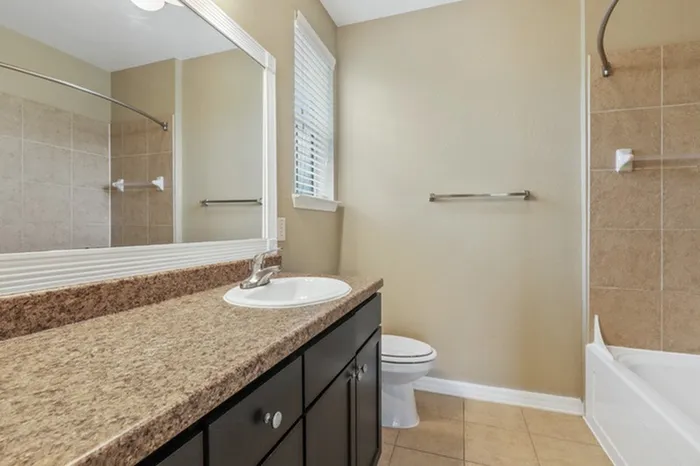 Image of a bathroom with a soaking tub, dark-colored cabinetry, and a window with natural sunlight above the toilet at Lantower Cypress Creek.
