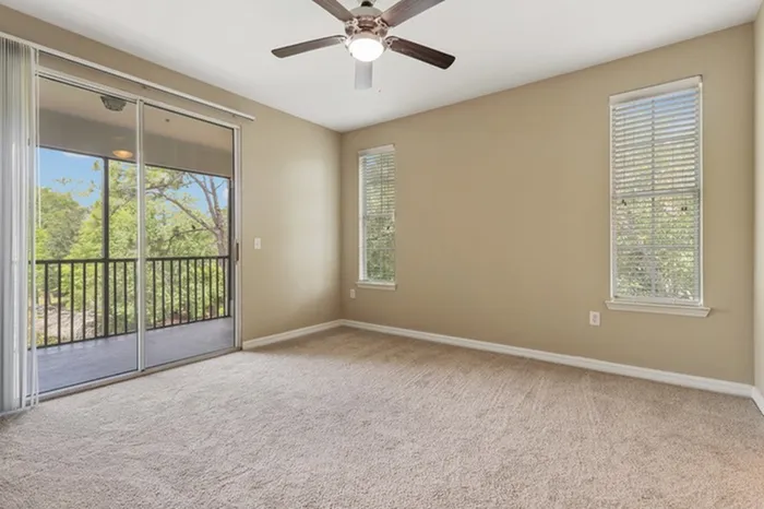 Image of a carpeted living room with two large windows and a door leading to a balcony at Lantower Cypress Creek.