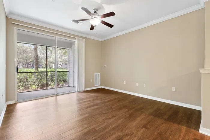 Image of a spacious living room with a ceiling fan, wood plank vinyl floors, and a sliding glass door to a balcony at Lantower Cypress Creek.