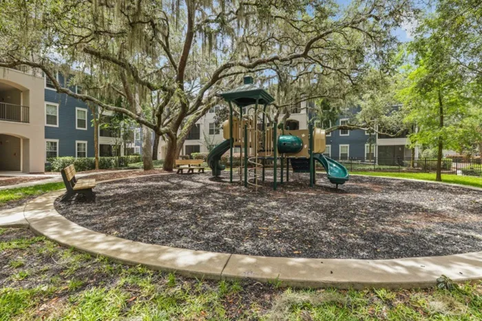 Image of a wood chip playground with a play structure and large tree at Lantower Cypress Creek.