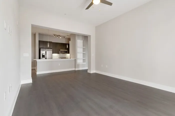 Spacious kitchen at Bullhouse with wood-style flooring, stainless steel, energy efficient appliances, quarts countertops, 10-12-foot ceilings, and tile backsplash and a spacious living room next to the kitchen.