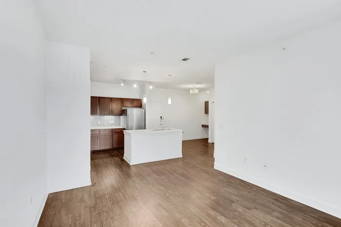 Spacious living room with ample room for seating, natural sunlight, and classic finishes with access to modern kitchen equipped with stainless steel appliances, large countertops, a floating island, and ample lighting at Lantower Ambrosio Apartments