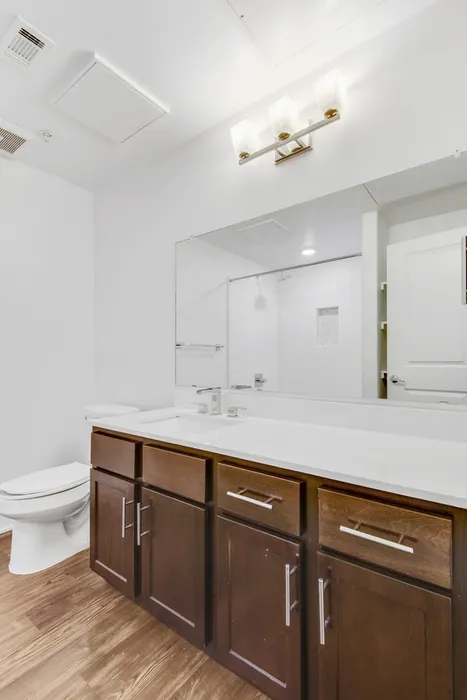 Modern bathroom, pristine white walls and countertop, wood cabinets, and wood flooring at Lantower Ambrosio Apartments