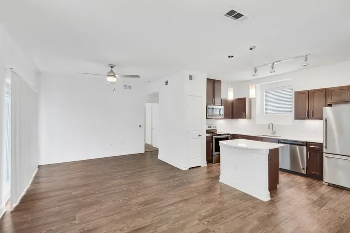 Spacious living room with ample room for seating, natural sunlight, and classic finishes with access to modern kitchen equipped with stainless steel appliances, large countertops, a floating island, and ample lighting at Lantower Ambrosio Apartments