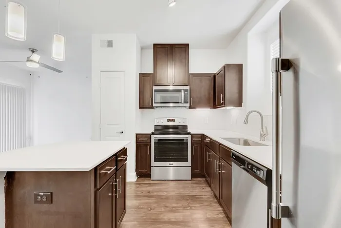 Modern kitchen equipped with stainless steel appliances, large countertops, a floating island, wood cabinets and ample lighting at Lantower Ambrosio Apartments.