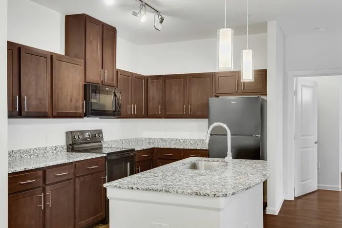 Modern kitchen equipped with stainless steel appliances, large countertops, a floating island, wood cabinets and ample lighting at Lantower Ambrosio Apartments.