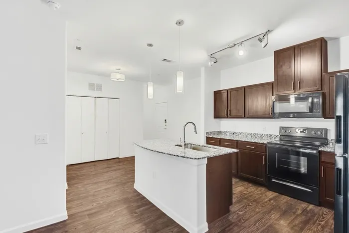 Modern kitchen equipped with stainless steel appliances, large countertops, a floating island, wood cabinets and ample lighting at Lantower Ambrosio Apartments.