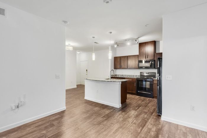 Spacious living room with ample room for seating, natural sunlight, and classic finishes with access to modern kitchen equipped with stainless steel appliances, large countertops, a floating island, and ample lighting at Lantower Ambrosio Apartments