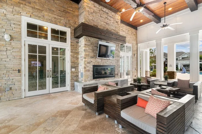 Covered patio with sofa chairs, a fire place, and wall-mounted TV at Patterson Place Apartments.
