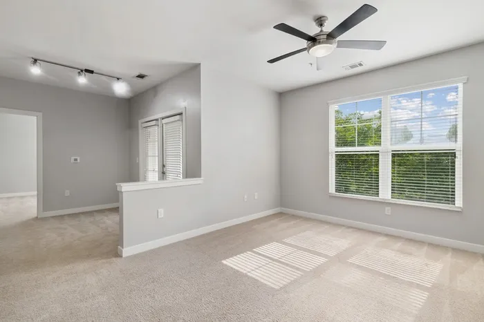 Carpeted living room with two large windows and a door leading to a balcony at Realm at Patterson Place.
