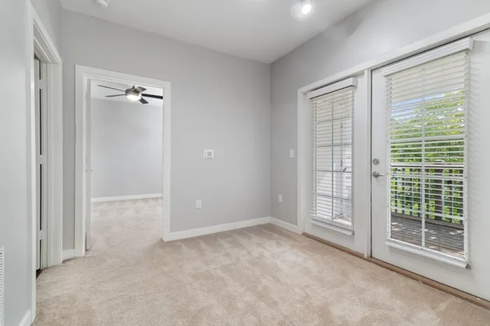 Bedroom with carpet, a ceiling fan, and white, French doors leading to a balcony at Patterson Place Apartments.