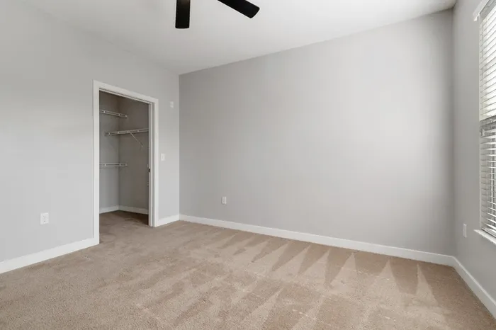 Carpeted bedroom with a ceiling fan, walk-in closet, and large window with natural sunlight at Realm at Patterson Place.