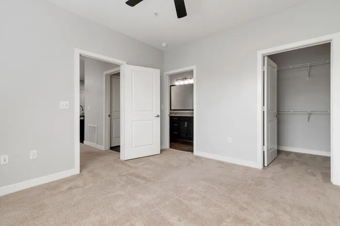 Carpeted bedroom with a ceiling fan, walk-in closet, and a private bathroom at Realm at Patterson Place.
