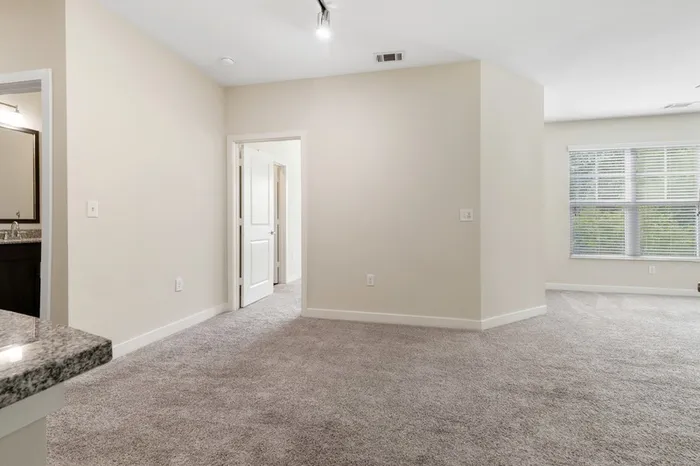 Carpeted living room with a large window and access to a bathroom at Realm at Patterson Place.