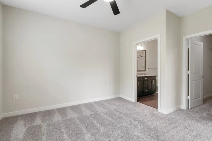 Carpeted bedroom with a ceiling fan, walk-in closet, and a private bathroom at Realm at Patterson Place.