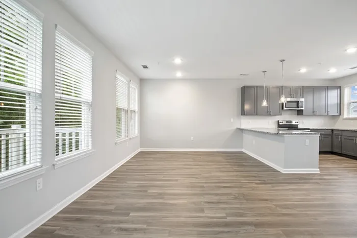 Kitchen at Lantower Garrison Park with wood-style flooring, granite countertops, tile backsplash, 10-foor ceilings, a kitchen island, and stainless steel, energy-efficient appliances and an attached, open-concept living room with large windows.