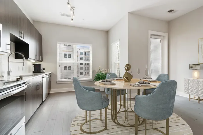 Large, open concept kitchen at Bullhouse with wood-style flooring, stainless steel, energy efficient appliances, white quarts countertops, a kitchen bar, and tile backsplash decorated with a coffee machine, house plant, gold kitchen table and blue plush chairs.