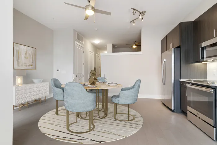 Large, open concept kitchen at Bullhouse with wood-style flooring, stainless steel, energy efficient appliances, white quarts countertops, a kitchen bar, and tile backsplash decorated with a coffee machine, house plant, gold kitchen table and blue plush chairs.