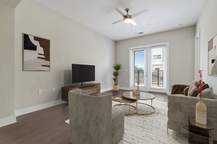 Living room with wood-style flooring, ceiling fan, glass doors leading to a private balcony, grey, modern furniture and a TV on a wooden stand at Bullhouse.