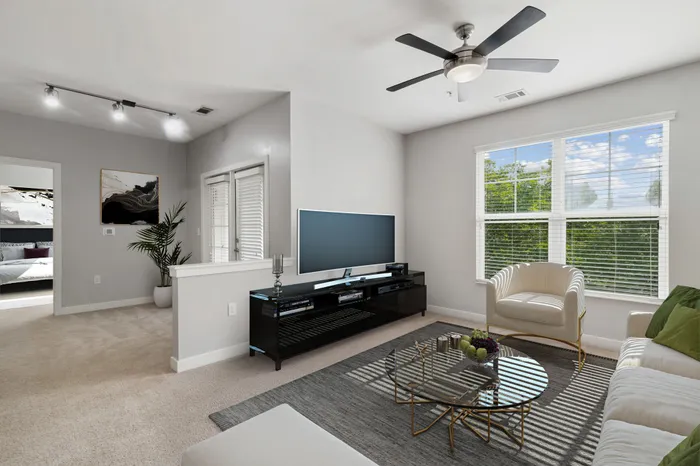 Carpeted living room with two large windows, 9-foot ceilings, access to a private balcony, modern furniture and a TV on a wooden stand at Realm at Patterson Place.