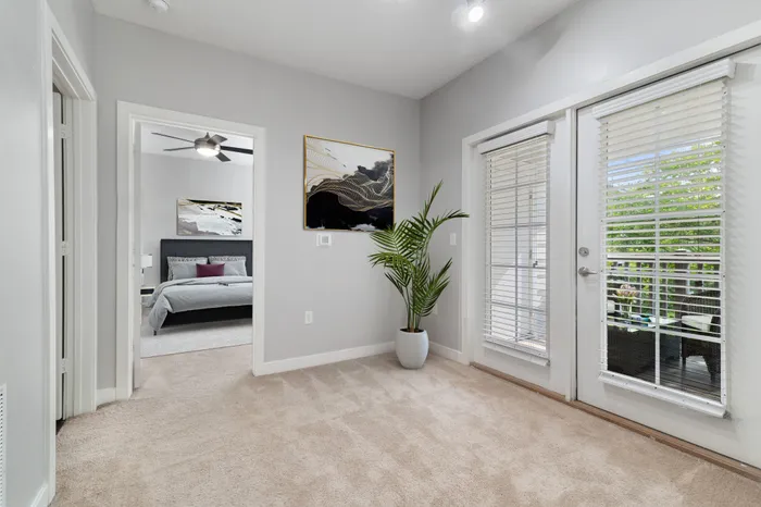 Bedroom with carpet, a ceiling fan, 9-foot ceilings, white, French doors leading to a private balcony, a large grey bed and modern wall art at Realm at Patterson Place Apartments.