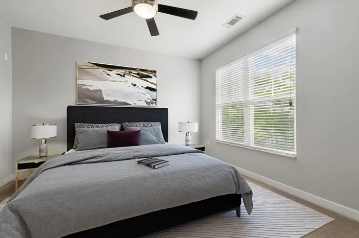 Bedroom with wood-style flooring, a ceiling fan, 9-foot ceilings, large windows, a large grey bed and modern wall art at Realm at Patterson Place Apartments.