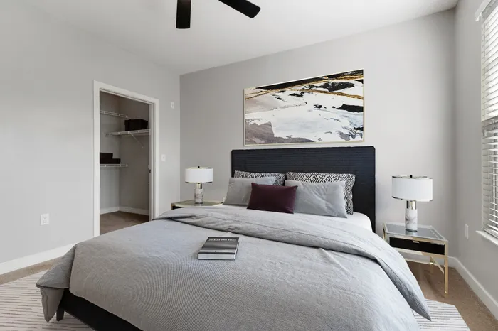 Bedroom with wood-style flooring, a ceiling fan, 9-foot ceilings, large windows, a large grey bed, modern wall art and an expansive walk-in closet at Realm at Patterson Place Apartments.
