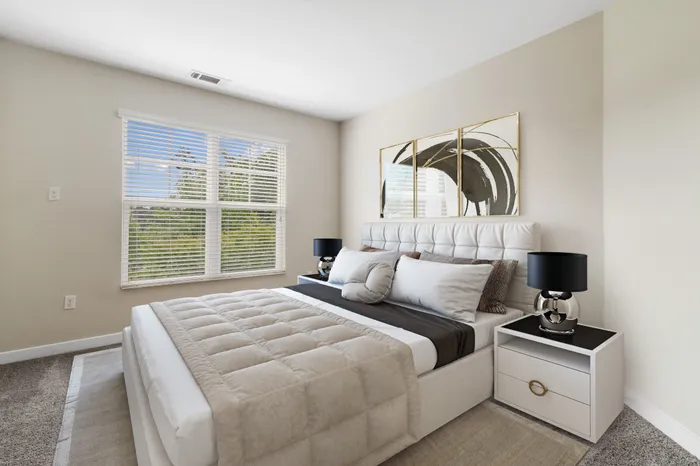 Bedroom with tan carpet, a ceiling fan, 9-foot ceilings, large windows, a large, cream bed with brown bedding and modern wall art at Realm at Patterson Place Apartments.