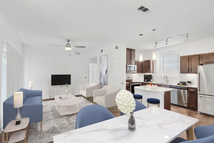 Spacious living room with ample room for seating, natural sunlight, and classic finishes with access to modern kitchen equipped with stainless steel appliances, large countertops, a floating island, and ample lighting at Lantower Ambrosio Apartments