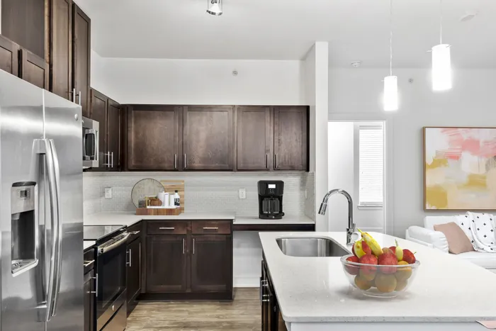 Modern kitchen fit with diamond white quartz countertops and stainless steel sink basin, stainless steel appliances, and an island with overhead lighting at Lantower Techridge apartments