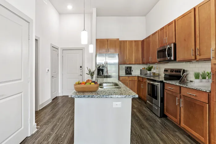 Kitchen with granite countertops, wood-style cabinets, stainless steel appliances, and a kitchen island in the middle at Lantower Legacy Lakes apartments