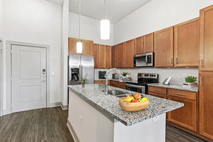 Kitchen with granite countertops, wood-style cabinets, stainless steel appliances, and a kitchen island in the middle at Lantower Legacy Lakes apartments