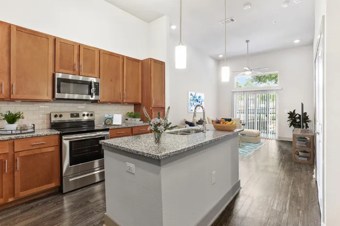 Kitchen with granite countertops, wood-style cabinets, stainless steel appliances, and a kitchen island in the middle at Lantower Legacy Lakes apartments