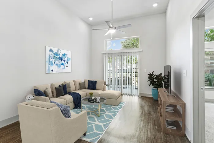 High ceiling room with ceiling fan, dark stained wood-style flooring, with glass sliding door providing natural lighting in Lantower Legacy Lakes' apartment