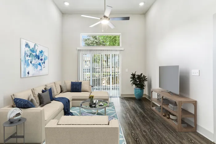 High ceiling room with ceiling fan, dark stained wood-style flooring, with glass sliding door providing natural lighting in Lantower Legacy Lakes' apartment