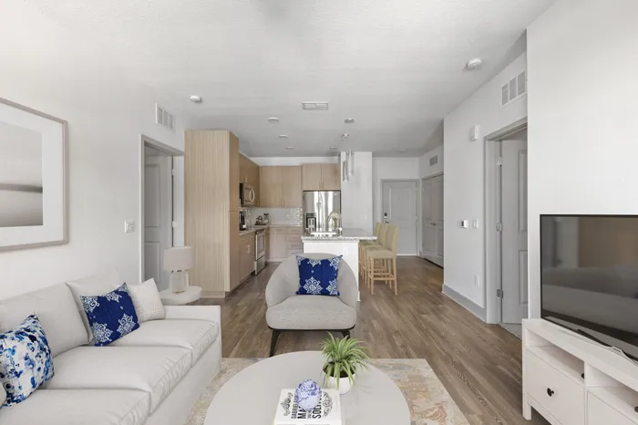 Kitchen with a side-by-side refrigerator, granite countertops, stainless steel appliances, and a kitchen island with an attached hard-wood floor living room decorated with simple cream couches, blue throw pillows and a TV with a white stand at Lantower Grande Flats.