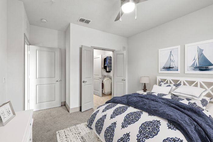 Carpeted bedroom with a large white bed, blue bedding and decorations and an area rug with lots of light and French doors leading to a closet at Lantower Grande Flats.