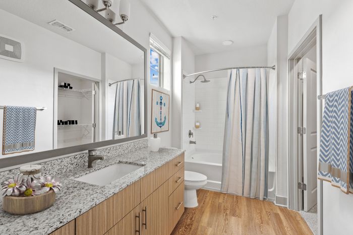Bathroom with grey, granite countertops and a spacious shower with a high window above the toilet at Lantower Grande Flats decorated in a Nautical theme with blue accents.