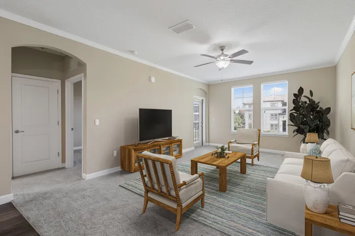 A carpeted, spacious living room with two large windows and a door leading to a balcony at Lantower Grande Pines decorated with wooden, modern furniture.