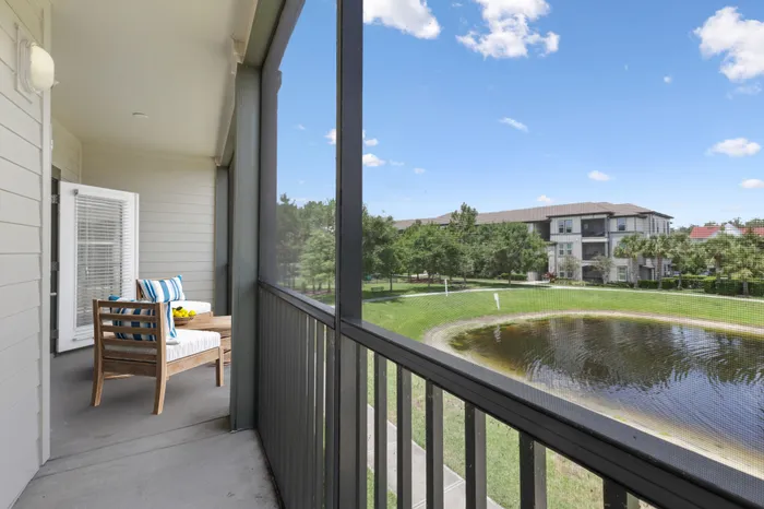 A long and spacious balcony with wooden railings, a wooden, white outdoor furniture set and a view of a pond and trees at Lantower Grande Pines.
