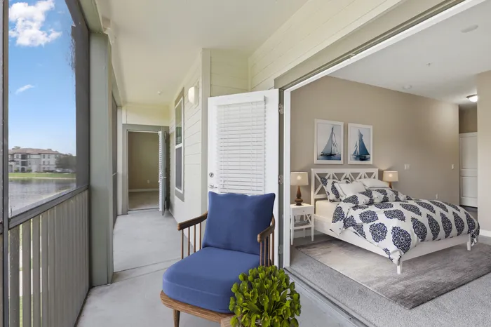 Long and spacious balcony with blue cushioned, wooden outdoor chair and a door to a carpeted bedroom with a large white bed at Lantower Grande Pines.