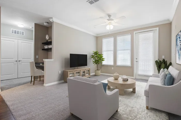 Carpeted living room with access to a private balcony, two large windows, modern, cream furniture and a TV on a wooden stand at Lantower Asturia.