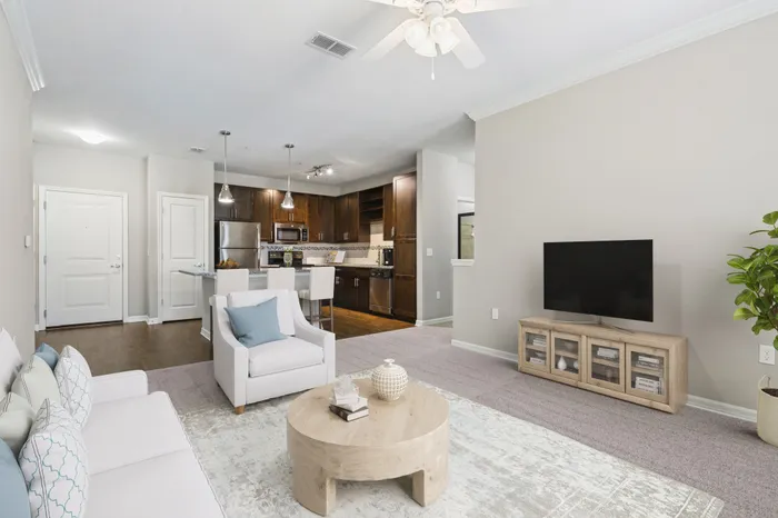 Energy-efficient kitchen with Luna Pearl granite countertops, stainless steel Whirlpool appliances, and a kitchen island with bar stools and a hard-wood floor living room the background with access to a balcony, modern, cream furniture and a TV on a wooden stand at Lantower Asturia.