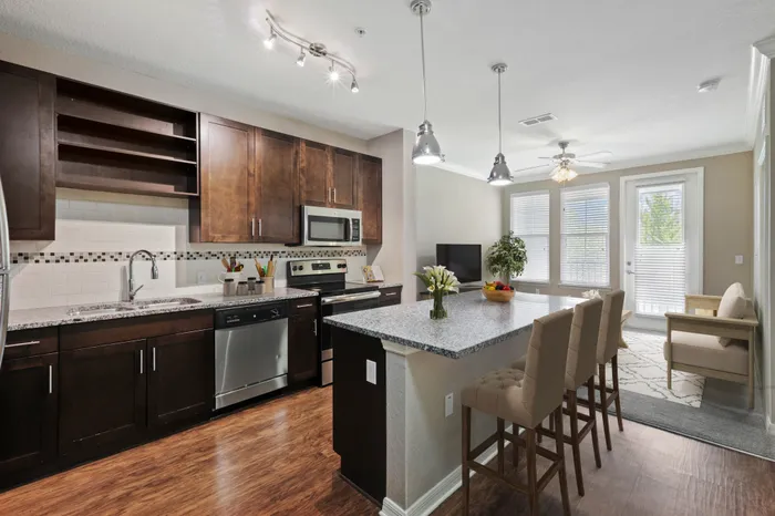 Kitchen with Luna Pearl granite countertops, wood-style plank floors, espresso custom cabinetry, a stainless-steel whirlpool appliance package, and tile backsplash with white bar stools, a bowl of fruit and a coffee machine at Lantower Asturia.