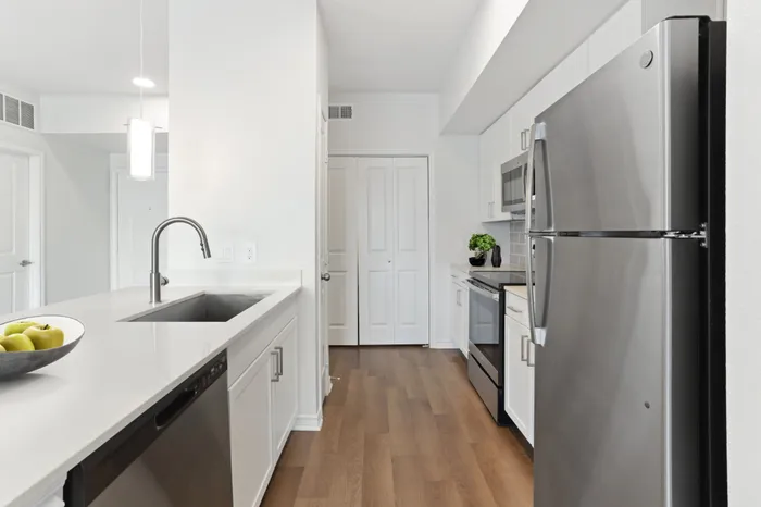 Modern kitchen fit with white countertops and stainless steel sink basin, stainless steel appliances, white cabinets and a counter with overhead lighting at Lantower Residences at the Collection